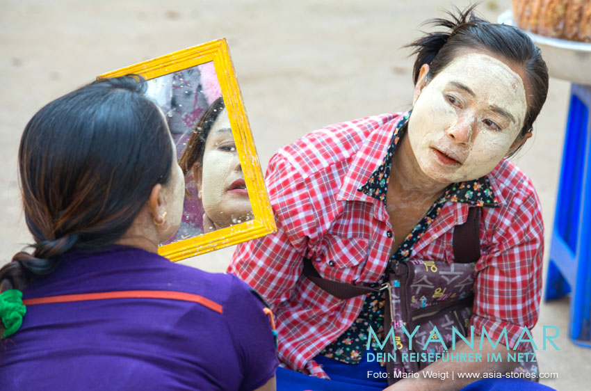 Eine Frau betrachtet sich im Spiegel, ob die Thanaka-Paste gut verteilt ist.