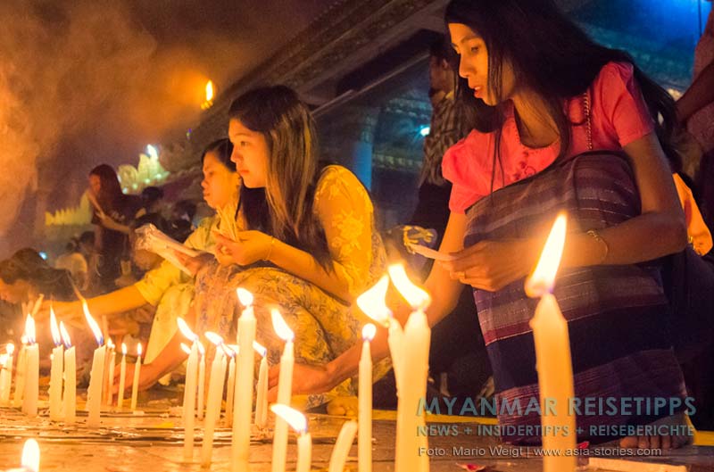 Frauen stellen in der Nähe vom Goldenen Felsen Kyaikhtiyo Kerzen für Buddha auf.