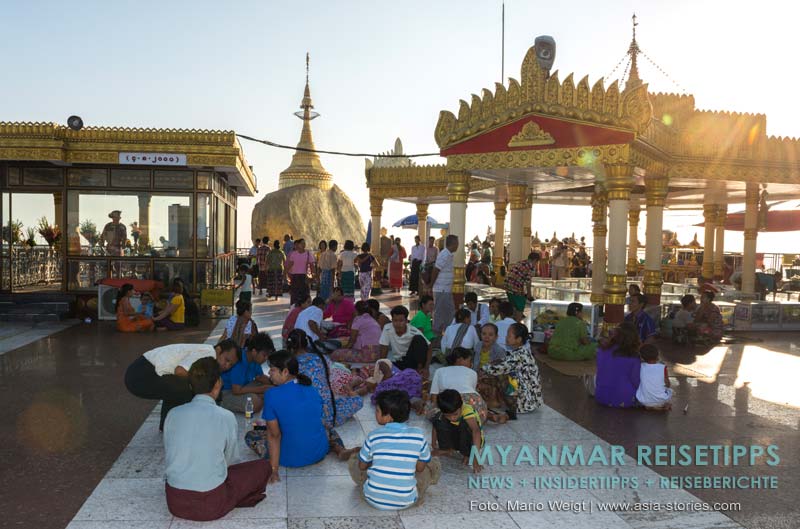 Pilger warten am Felsen. Auf den kühlen Steinfliesen vor dem Goldenen Felsen Kyaikhtiyo lässt es sich gut in der Nachmittagshitze aushalten.