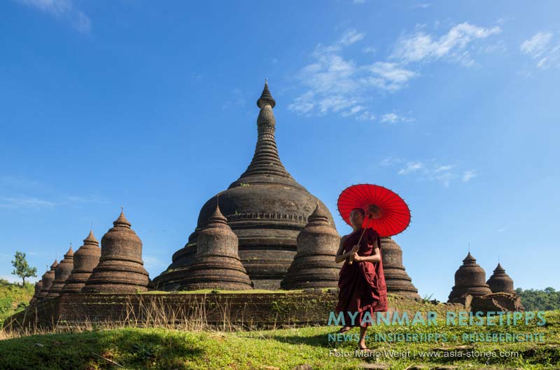 Mönch mit einem roten Bambusschirm vor der Ratanabon-Pagode in Mrauk U