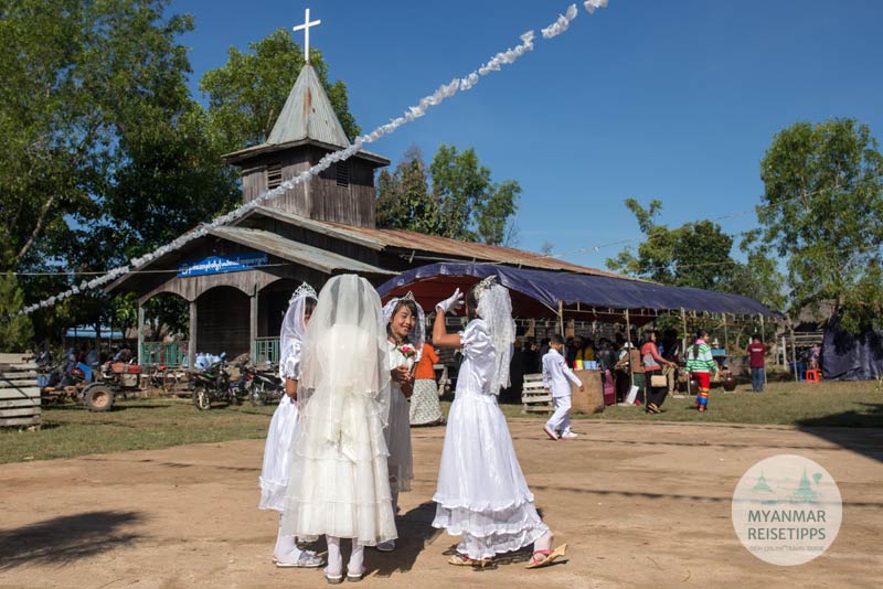 Mädchen in weißen Kleidern treffen sich zur Weihnachtsmesse vor einer kleinen Holzkirche in Loikaw