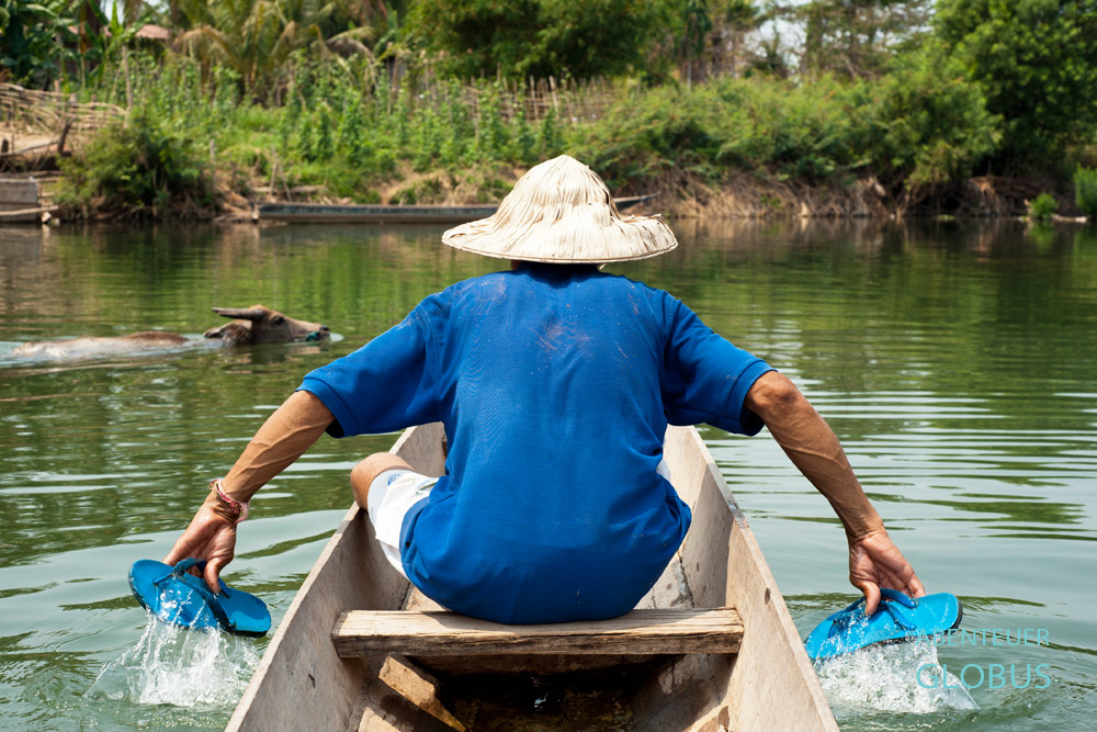 Ein Laote paddelt mit Flip-Flops nach Hause zur Insel Don Det in Si Phan Don in Laos. Wasserbüffel schwimmt durch den Mekong.