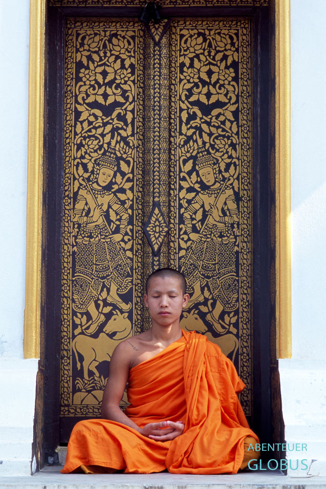 Meditierender Mönch vor einer Klostertür in Luang Prabang, dem buddhistischen Zentrum von Laos.