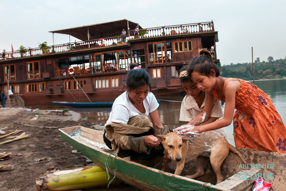 Im Dorf Ban Hung Noi bei Pakse legt das Boutique-Schiff Mekong Islands an. Davor wäscht eine Mutter mit ihren Töchtern einen Hund.