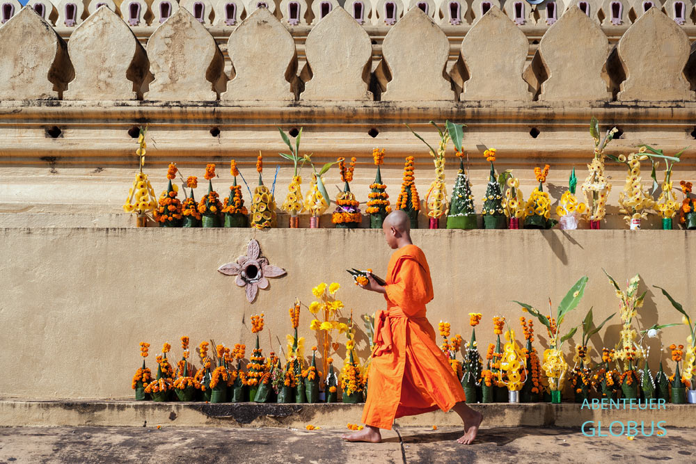 Novize stellt gespendete Blumengestecke am Stupa des That-Luang-Tempels zum Boun That Luang Fest in Vientiane, Laos, auf.