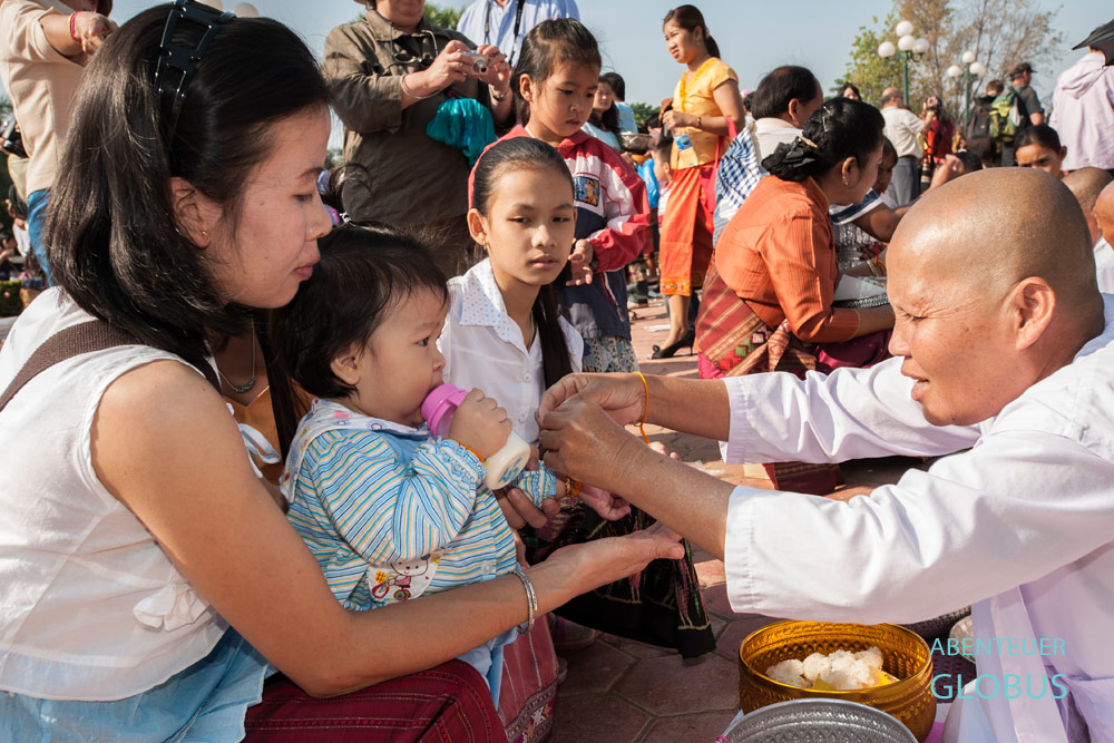Zum That Luang Fest in Vientiane bindet eine Nonne ein Bändchen um das Handgelenk und spricht ein Gebet.