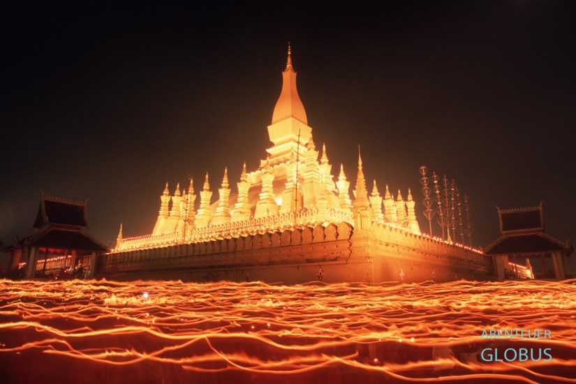 Am Vollmondabend umrunden Mönche und Gläubige den goldenen Stupa That Luang in Vientiane mit Kerzen, die Lichtstreifen erzeugen