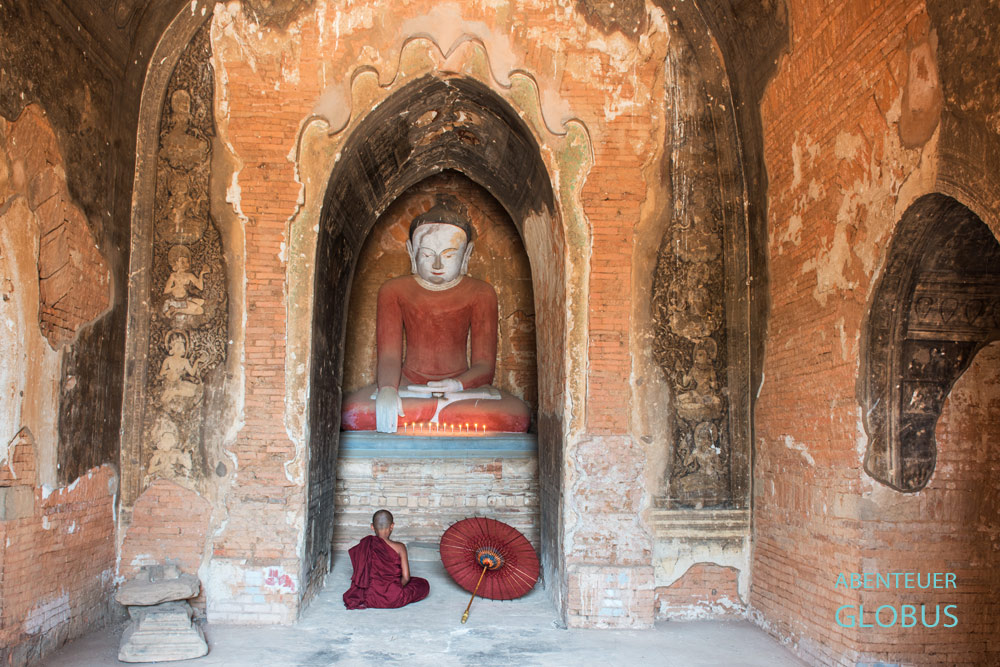 Meditierender Mönch vor einem sitzenden Buddha in einer buddhistischen Pagode mit Wandmalereien in Bagan.