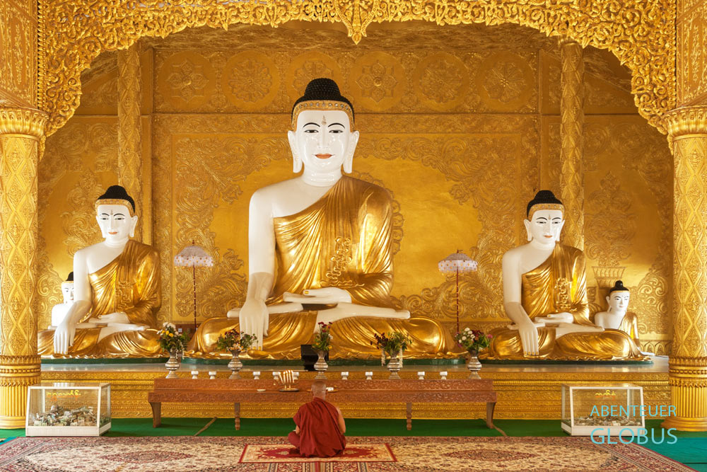 Ein Mönch meditiert vor goldenen Buddha-Statuen in der Shwemokhtaw-Pagode in Pathein in Myanmar.