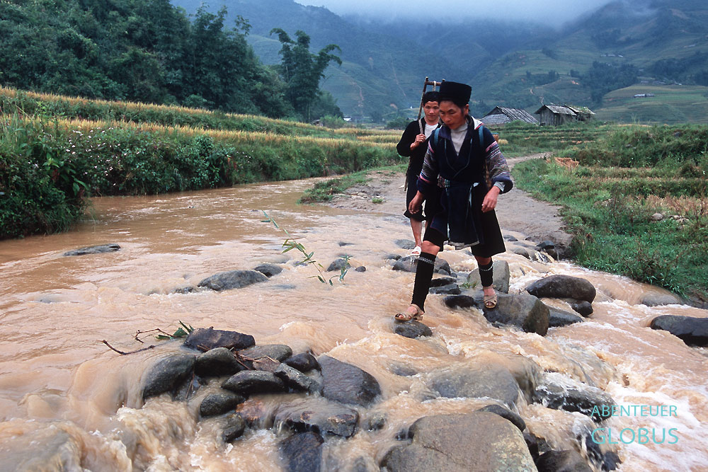 Zwei Personen der Volksgruppe Black Hmong durchqueren einen Fluss.