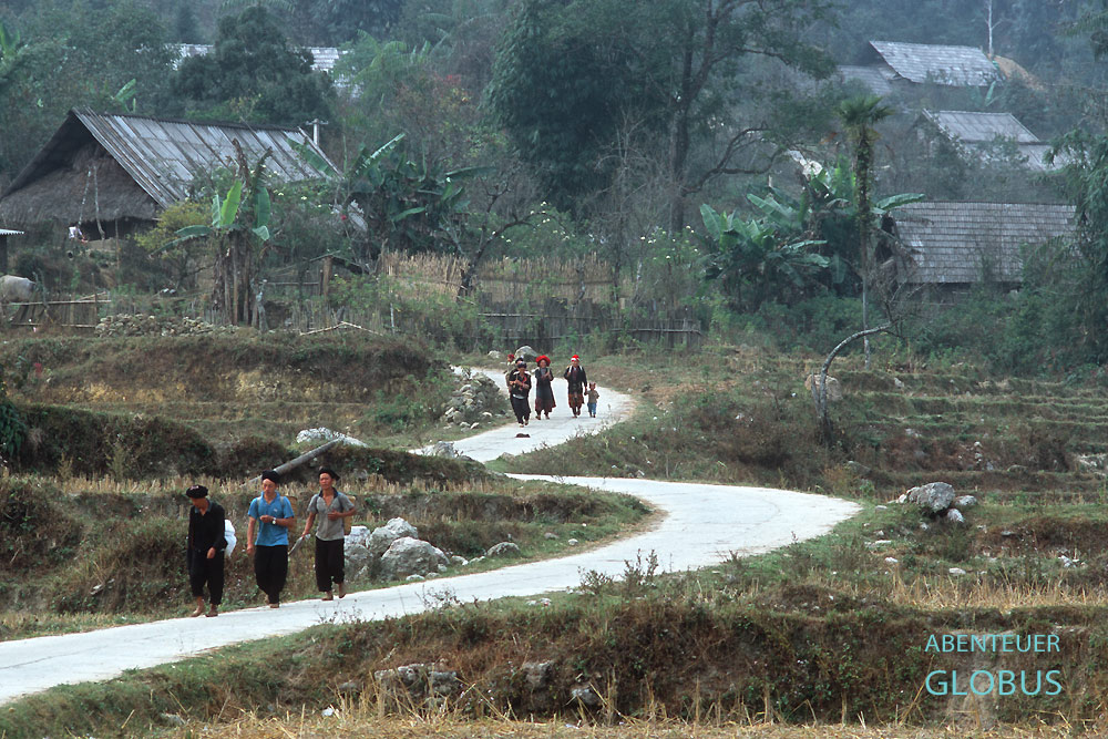 Einheimische laufen auf einem asphaltierten Weg durch das Bergdorf Taphin in Nordvietnam