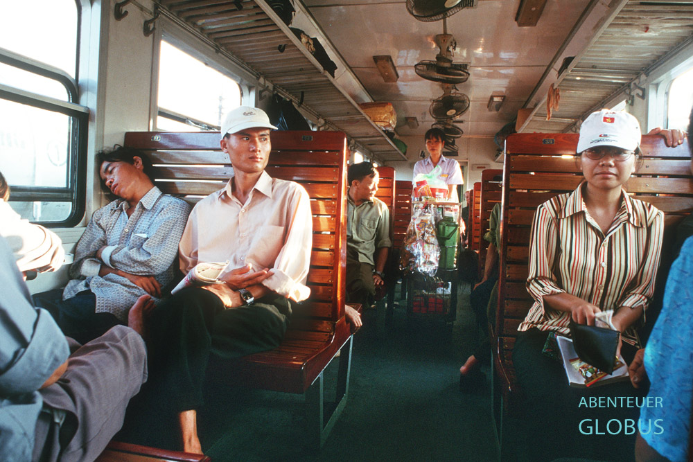 Passagiere auf Holzbänken im Zug von Hanoi nach Sapa, im Hintergrund eine Verkäuferin mit Getränkewagen