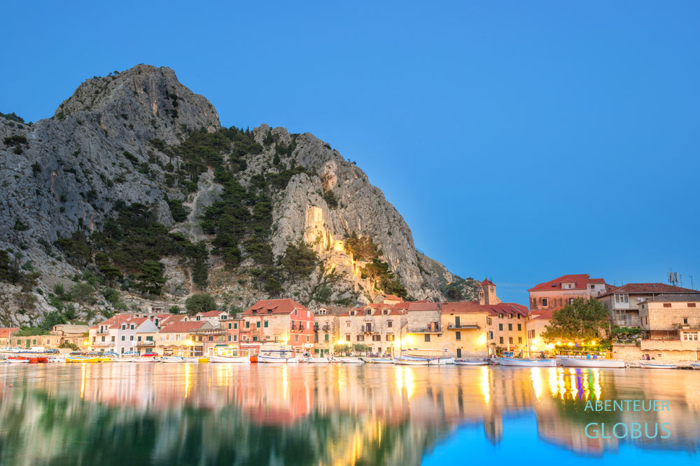 Abendaufnahme von Omis mit Altstadt und Burg Peovica am Fluss Cetina in Kroatien