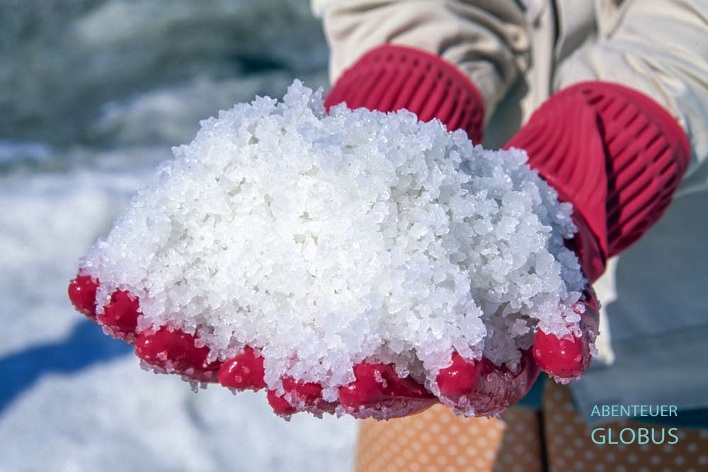 Eine Frau in den Salzfeldern von Kep zeigt frisch gewonnenes Meersalz.
