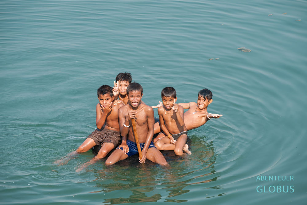 Fünf Jungen sitzen lachend auf einem Lkw-Schlauch im Mekong vor der Insel Don Det, Laos.