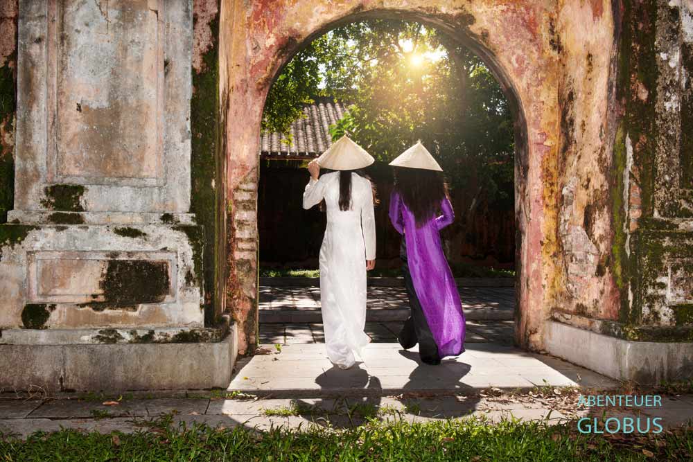 Ein Tor der alten Zitadelle durch das zwei Frauen im Ao Dai Gewand gehen