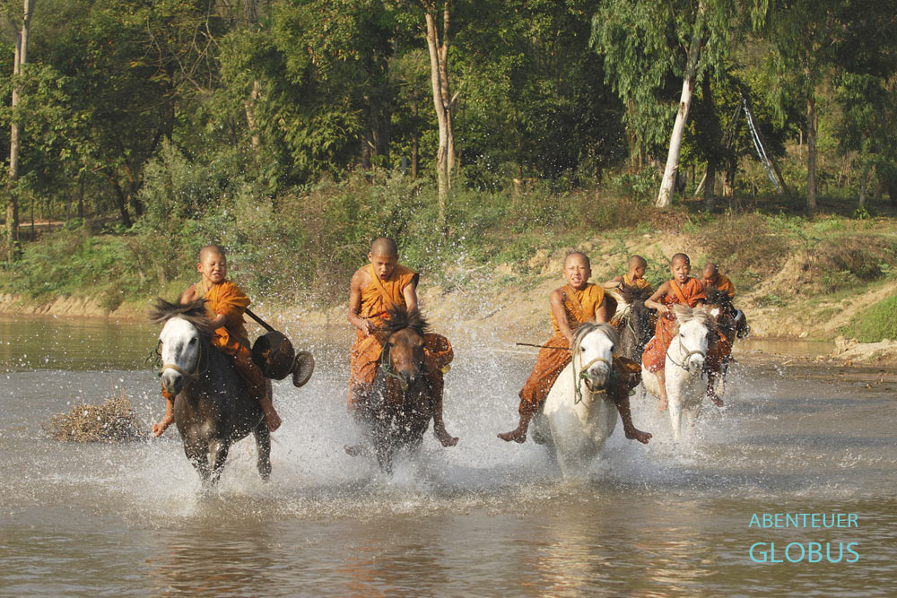 Novizen reiten durch den Fluss Mae Kham zum Pferdetempel Wat Tham Pa Archa Thong, auch Golden Horse Monastery genannt.