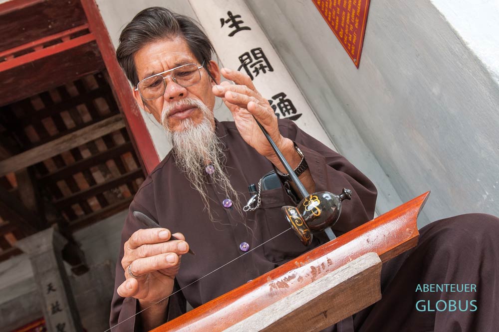 Priester mit Zither Dan bau im Thai Vi Tempel bei Ninh Binh