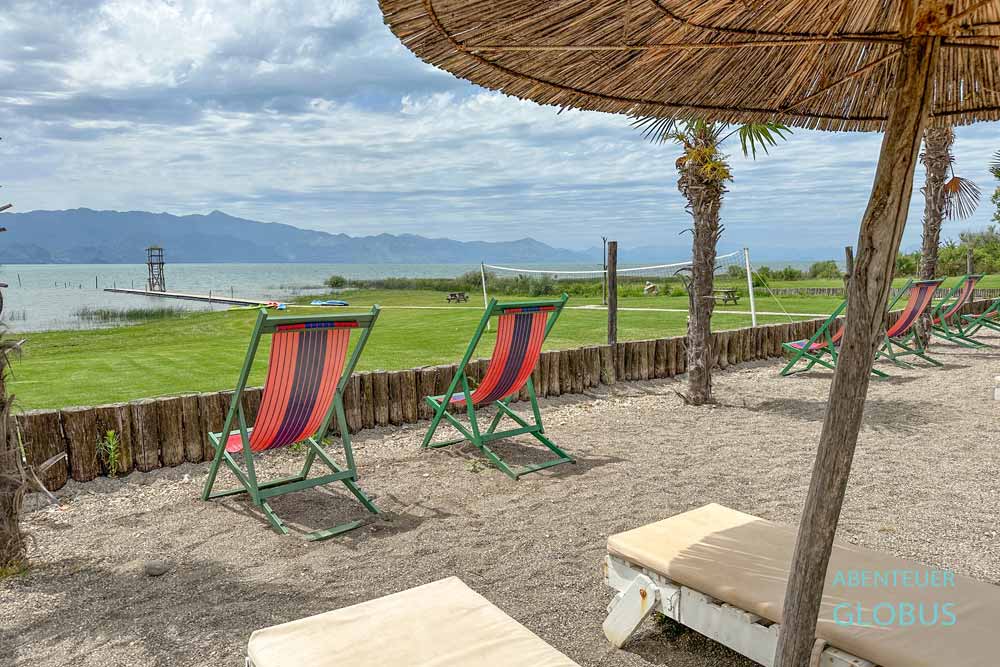 Strand mit Liegestühlen und Sonnenschirmen im Lake Shkodra Resort