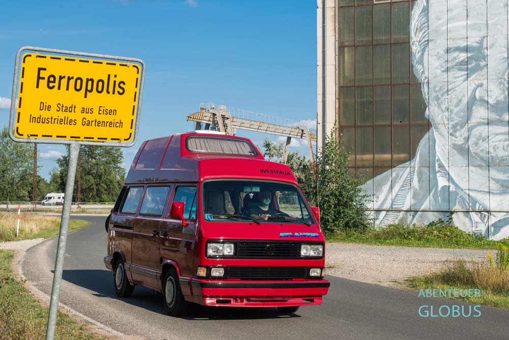 Roter VW T3 Atlantic auf der Straße neben dem Ortseingangsschild von Ferropolis in Gräfenhainichen
