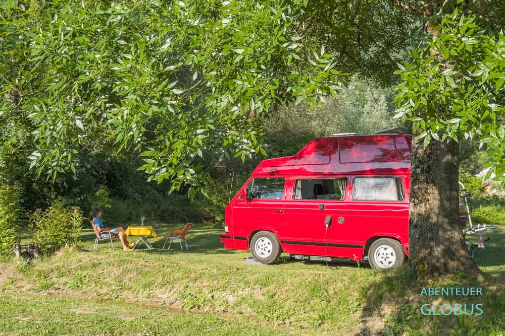 Eine Camperin sitzt vor einem roten Bulli auf dem Campingplatz Camping Status Quo in Kulen Vakuf.