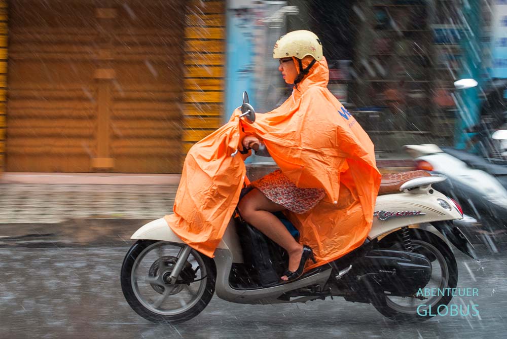 Eine Frau fährt Roller bei einem starken Regenschauer während der Regenzeit in Kambodscha.