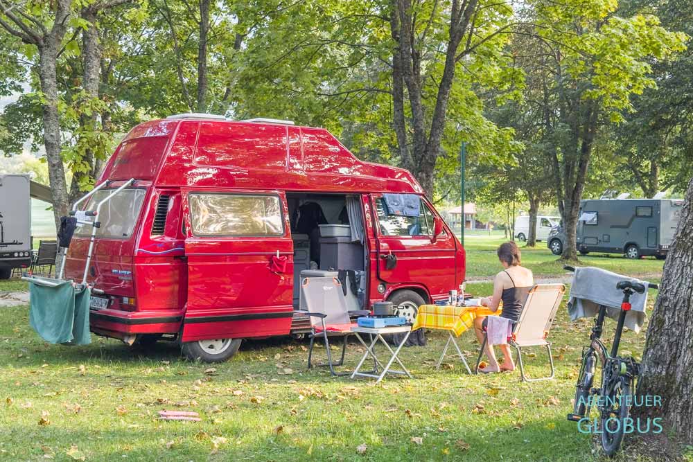 Einige Camper stehen unter Laubbäumen auf dem Campingplatz Autocamp Plivsko Jezero in Jajce.