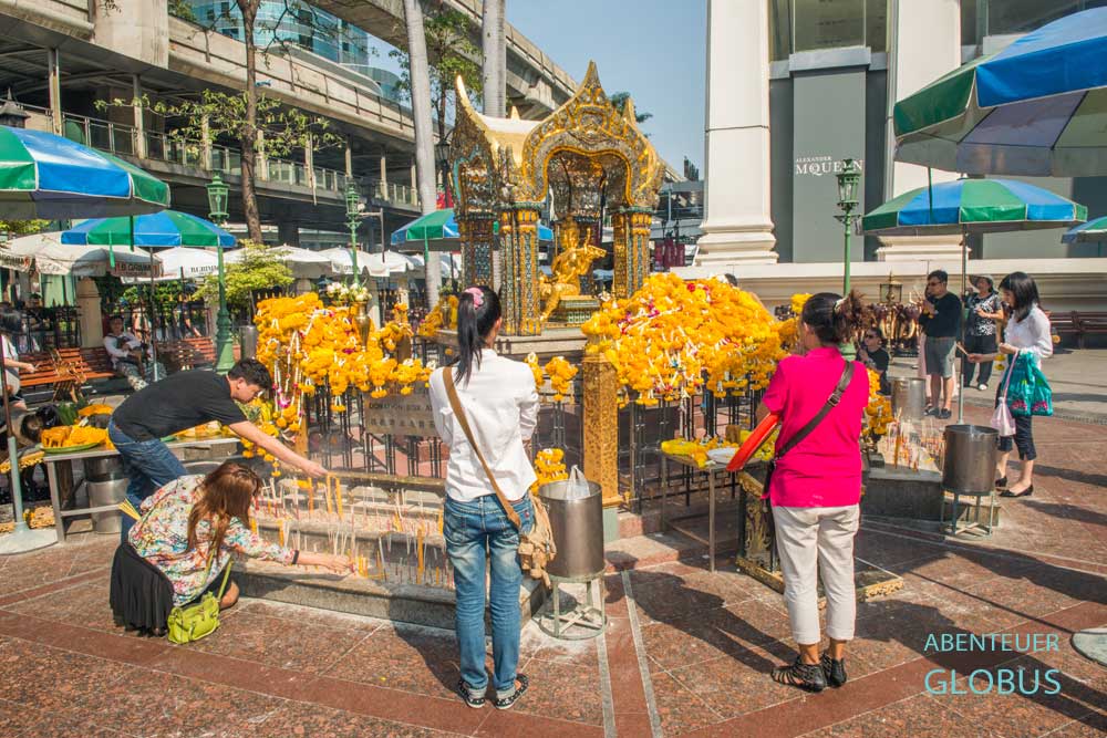 Betende Thais am Erawan-Schrein in Bangkok, die Kerzen anzünden und Blumenspenden darbieten.