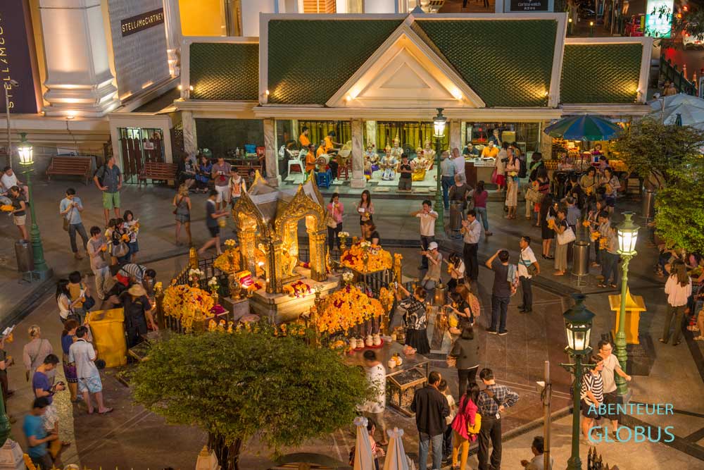 Der beleuchtete Erawan-Schrein in Bangkok am Abend mit Besuchern.