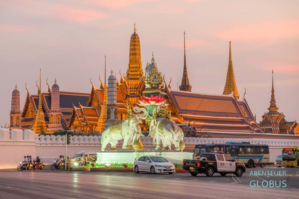 Abendlich beleuchteter Grand Palace in Bangkok, im Vordergrund fließender Verkehr