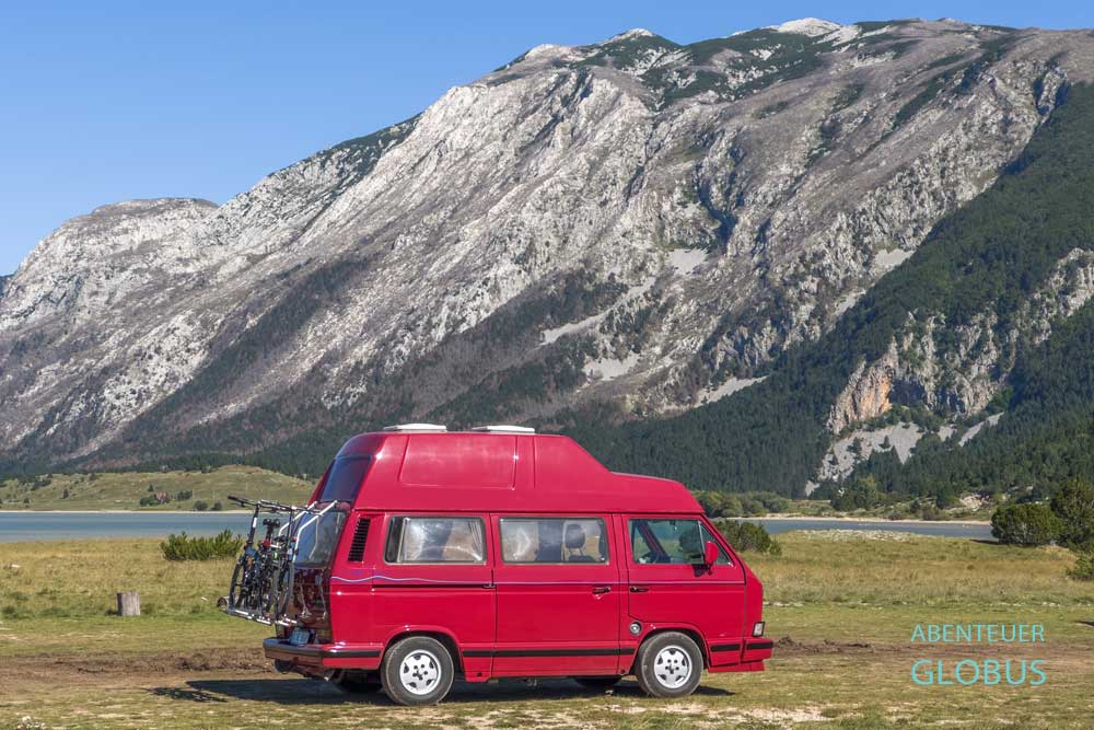 Im Naturpark Blidinje am Fuße des Blidinje-Sees erhebt sich das Cvrsnica-Gebirge. Davor parkt ein roter Bulli im Camp Blidinje.