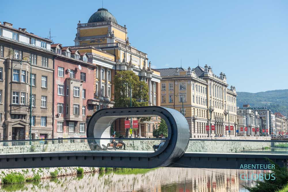 Brücke mit der Welle Festina Lente über den Fluss Miljacka und Prachtbauten aus der österreichisch-ungarischen Zeit