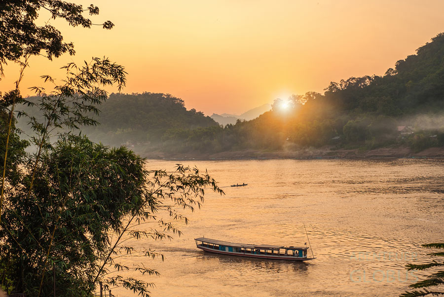 Sonnenuntergang in Luang Prabang mit einem Longtailboot im Vordergrund auf dem Mekong.