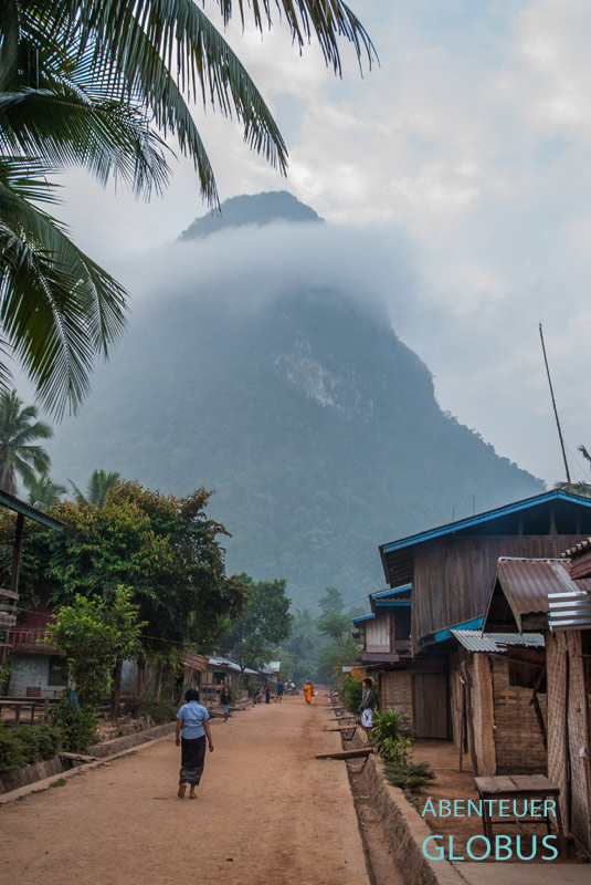 Hauptstraße von Muang Ngoy mit buddhistischen Mönchen beim morgendlichen Almosengang.