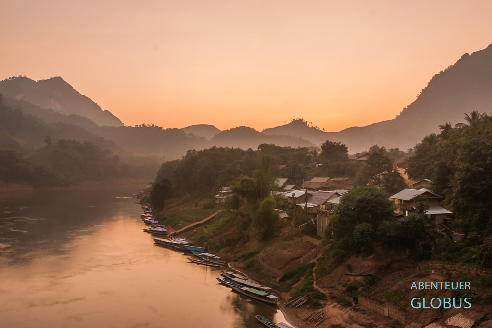 Nong Khiaw nach Sonnenuntergang: Fluss, Berge und Stadt in warmem orangefarbenem Licht.