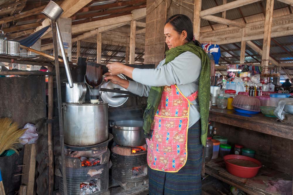 Eine Frau bereitet auf dem Markt in Nong Khiaw einen Kaffee Lao zu.