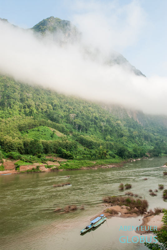 Fluss Nam Ou mit einem blauen Longtailboot und wolkenverhangener Karstberg