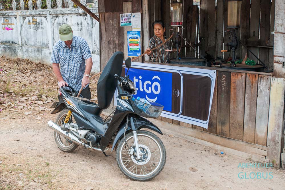Tourist betankt einen Motorroller mit Benzin an einer kleinen Pumpstation in Laos.
