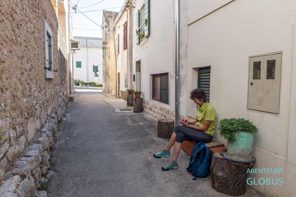 Eine Touristin auf einer Bank in einer Altstadtgasse in Sveti Filip i Jakov