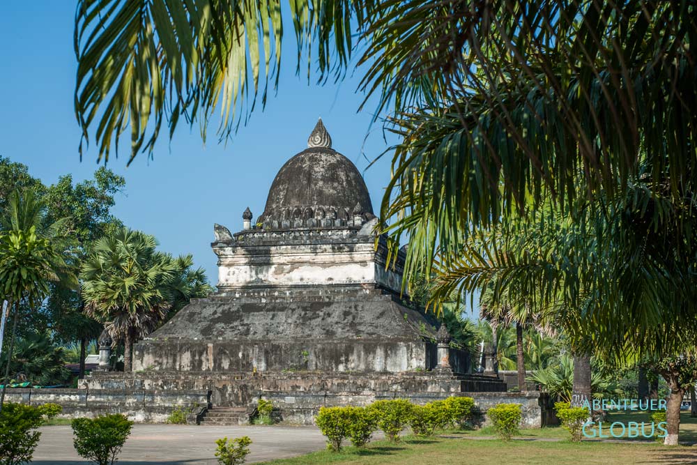 Wat Wisunarat mit blauem Himmel in Luang Prabang, im Vordergrund Palmen.