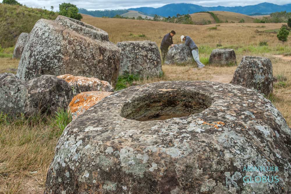 Steinkrug in Nahaufnahme auf der Ebene der Tonkrüge, zwei Männer blicken im Hintergrund in einen Krug.