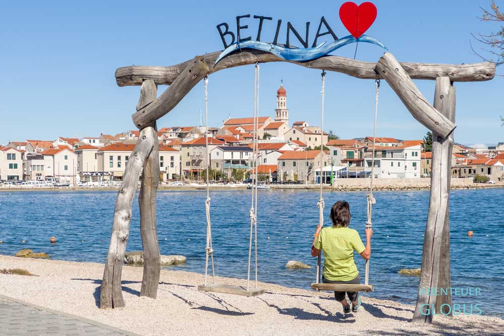 Urlauberin auf einer Schaukel mit Blick auf die Altstadt vom Ort Betina auf der Insel Murter