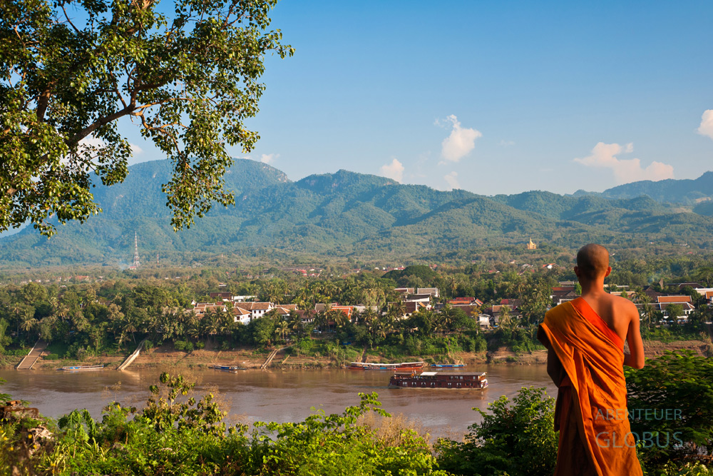 Buddhistischer Mönch blickt vom Wat Chomphet auf Luang Prabang und den Mekong mit einem Kreuzfahrtschiff.