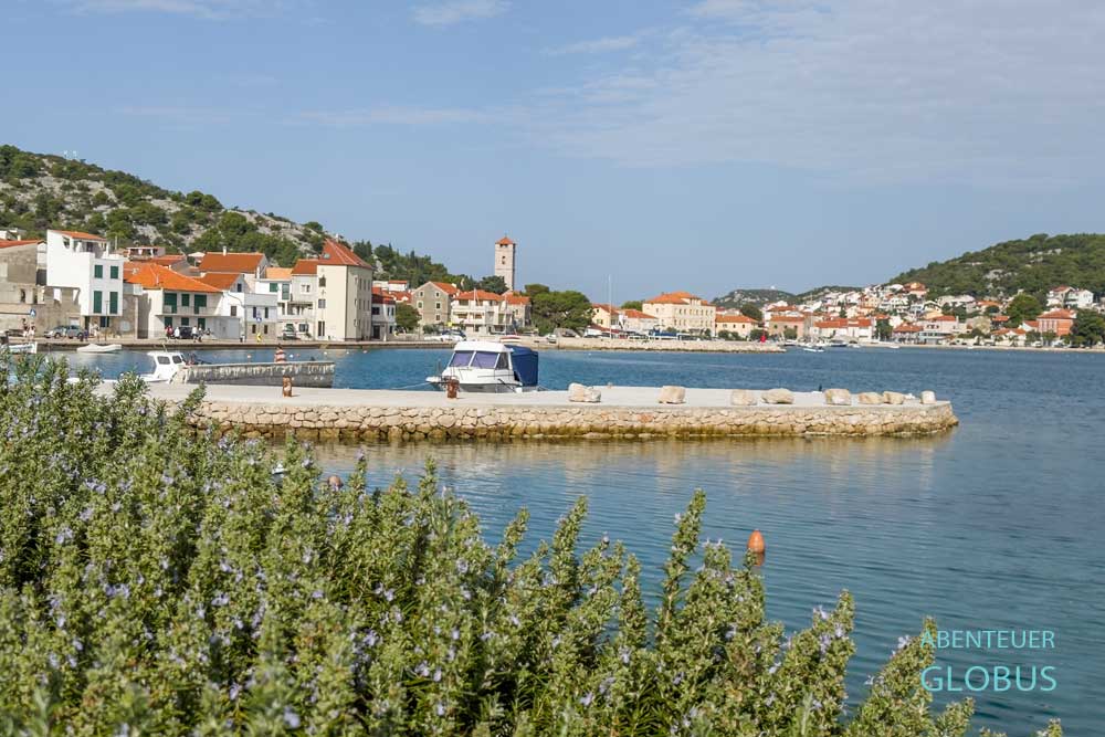 Betonpier mit Boot im Vordergrund, dahinter der Ort Tisno auf der Insel Murter in Kroatien
