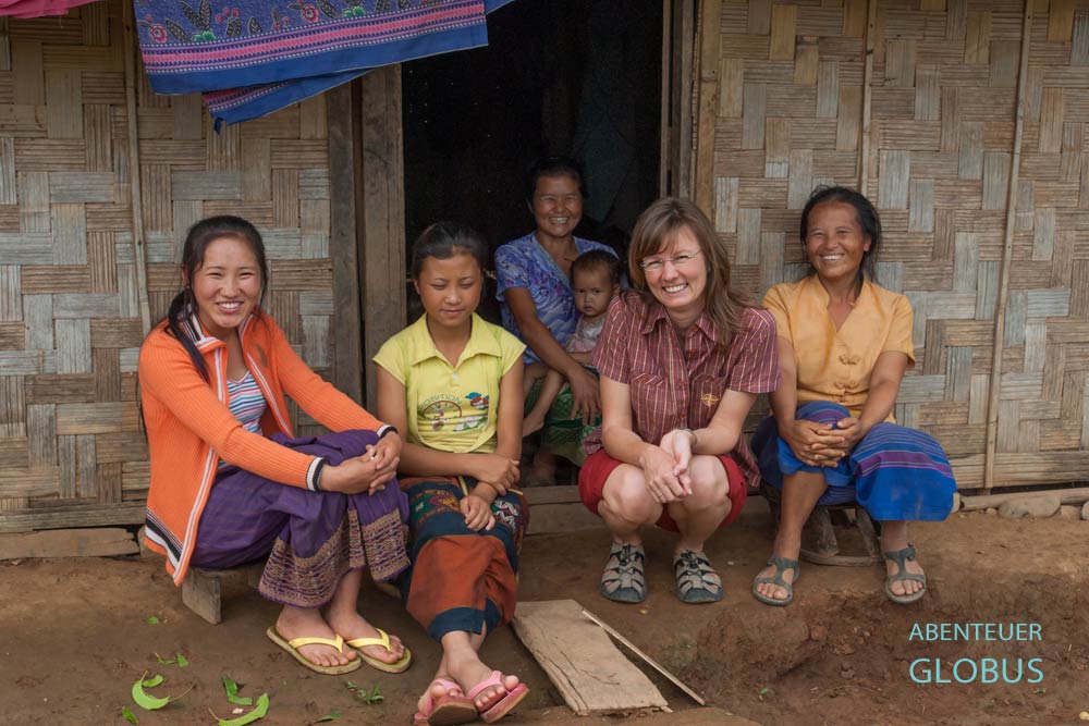 Touristin und einheimische Frauen sitzen vor einem Hauseingang in Phonsavan.