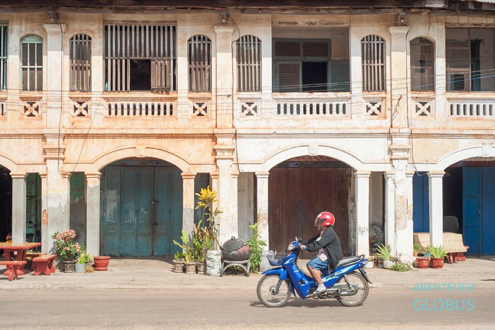Rollerfahrer fährt an einem Haus in Phonsavan vorbei.