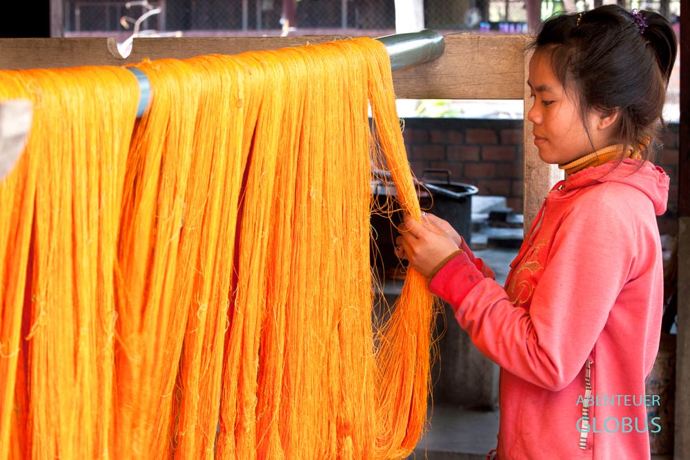 Frau kontrolliert orange gefärbte Seidenfäden in der Seidenmanufaktur Mulberries in Phonsavan.