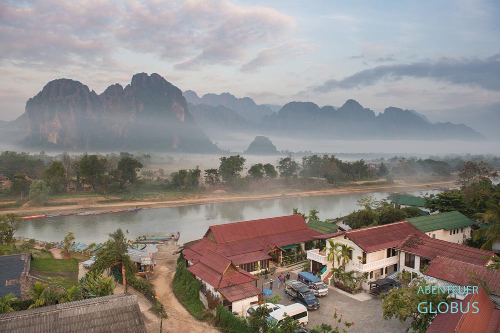 Karstberge im Morgennebel mit einem Hotel am Fluss Nam Song im Vordergrund in Vang Vieng
