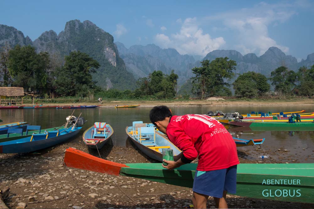 Fischer lackiert sein Boot am Fluss Nam Song in Vang Vieng, im Hintergrund Karstfelsen