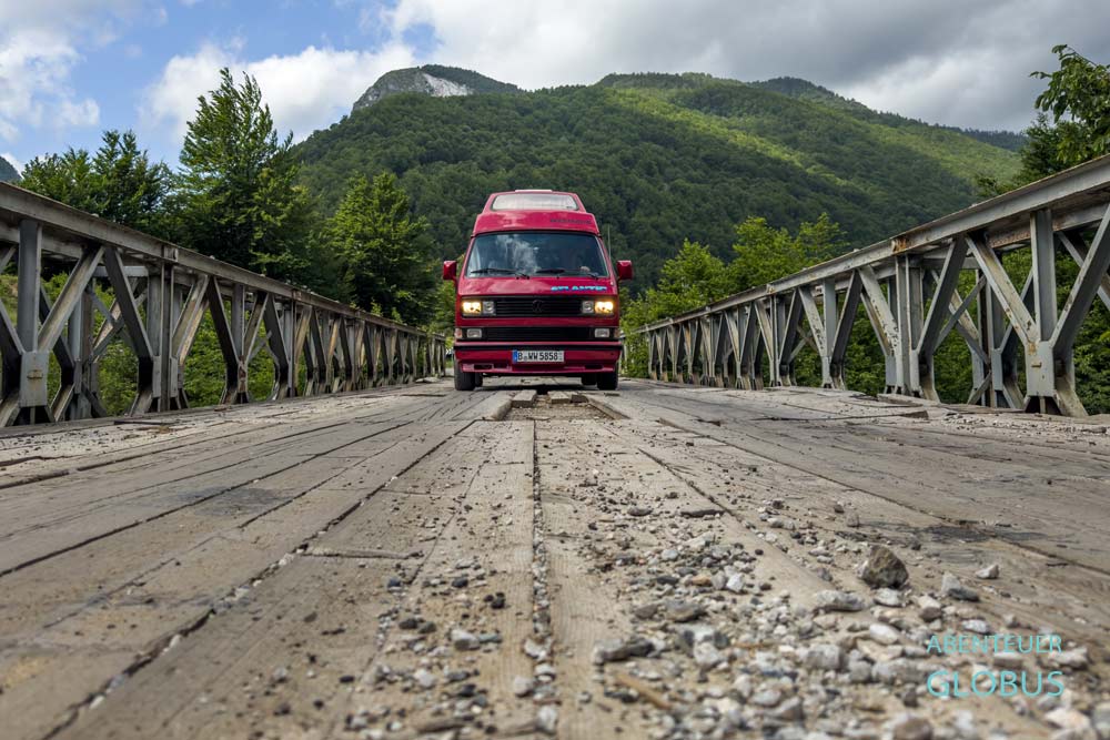 Wohnmobil fährt mit Abblendlicht über eine Holzbrücke in Albanien.